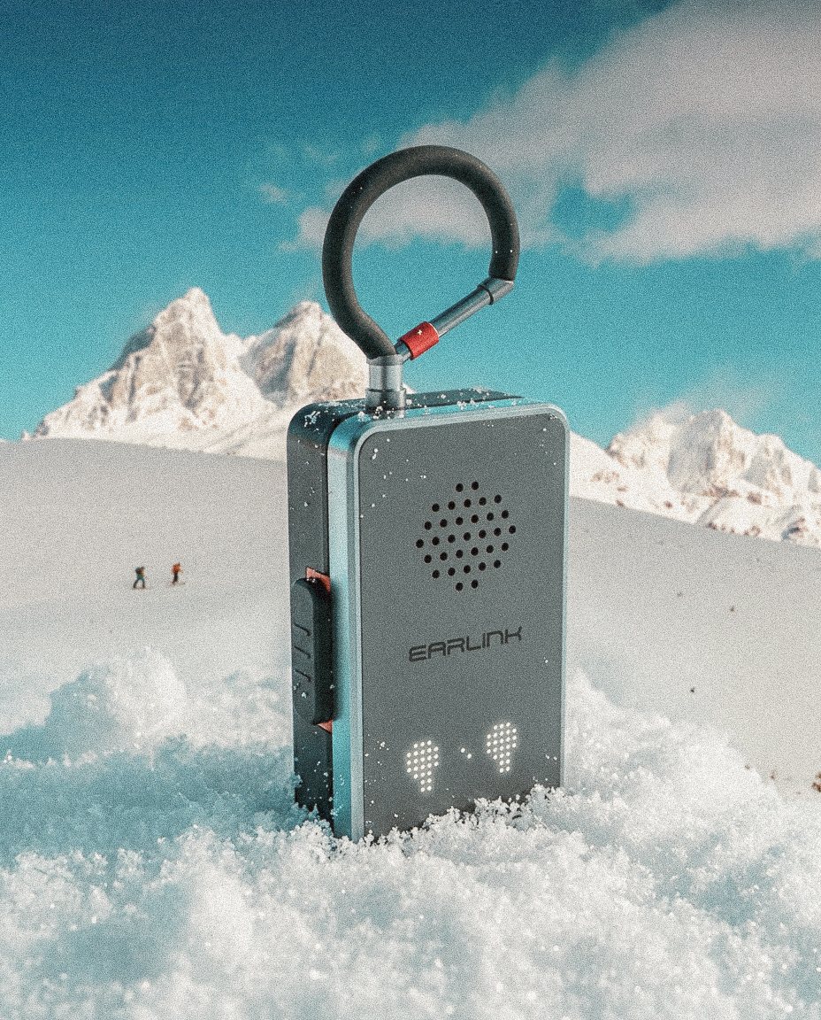 EarLink radio planted in fresh snow, carabiner antenna up, snowy peaks behind