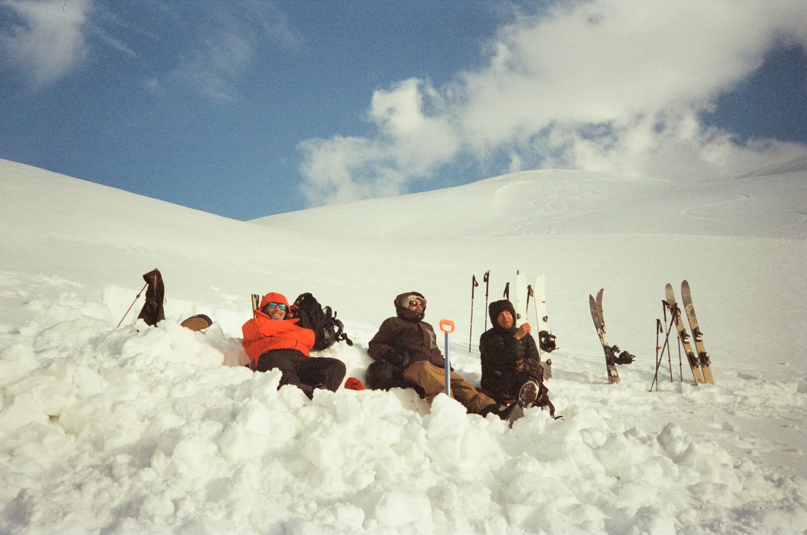 Crew sitting in the snow on a ridge, skis planted around