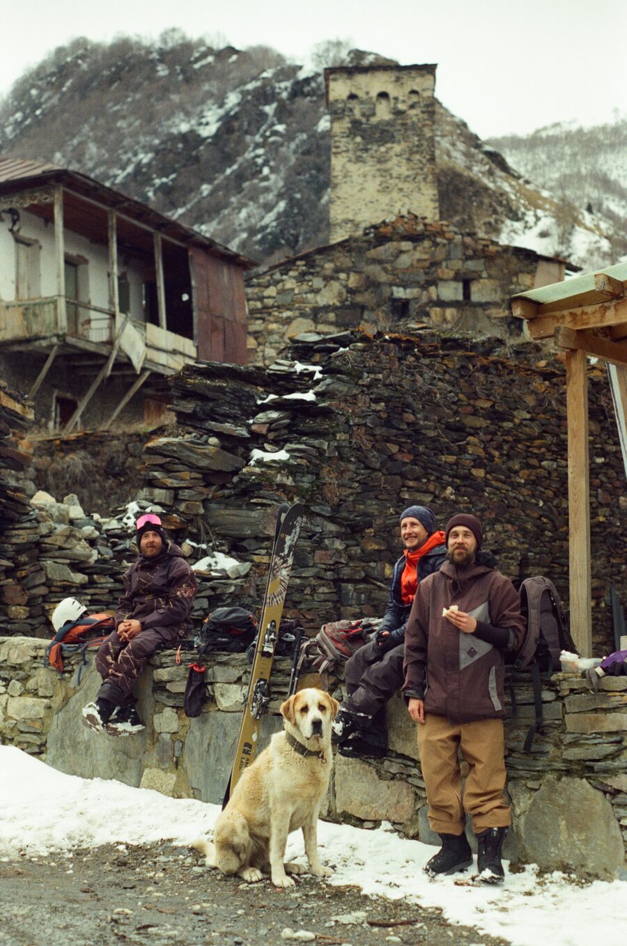 Crew and a dog resting under an old stone tower in a mountain village